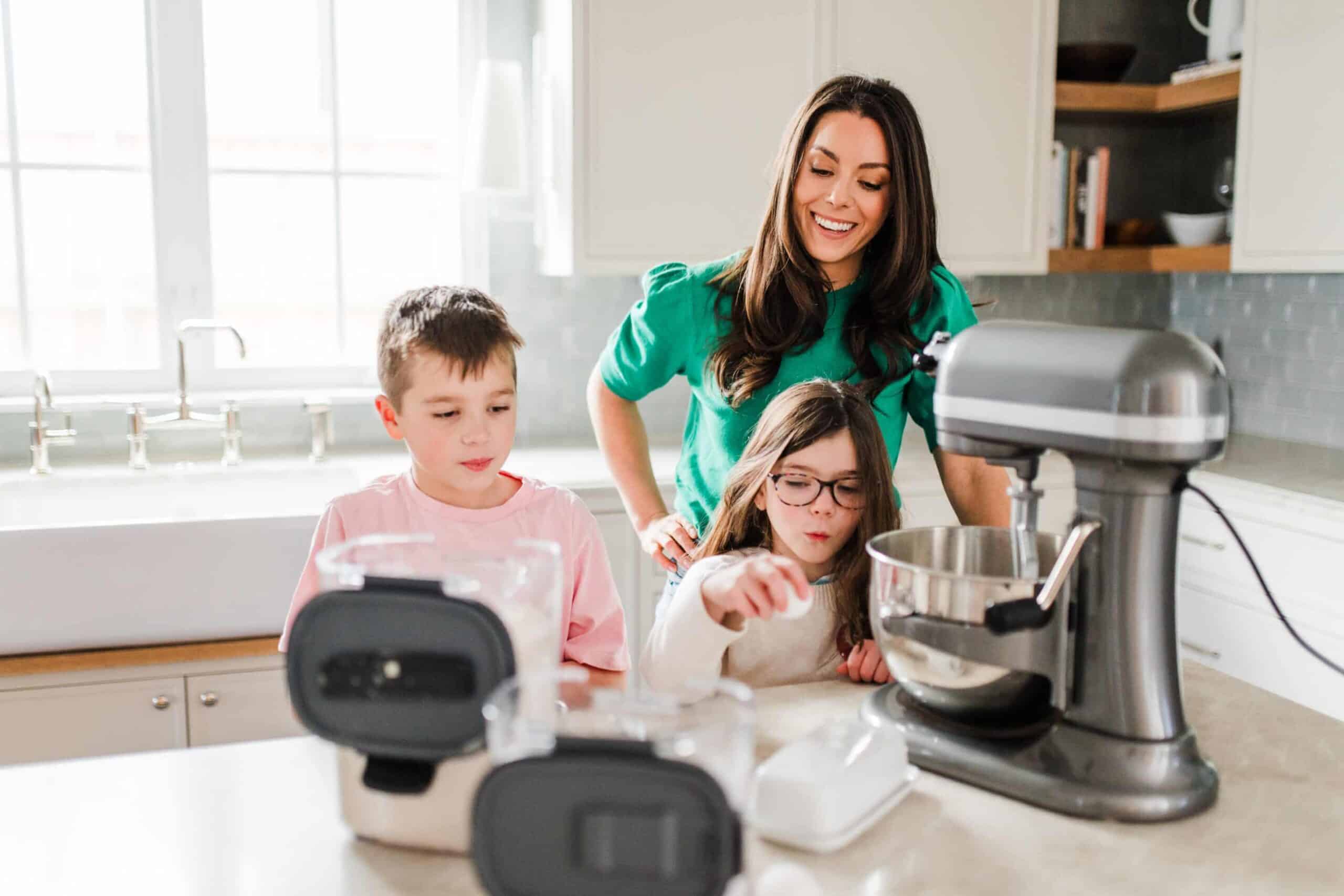 A mother and two children baking together in a bright kitchen with a stand mixer.