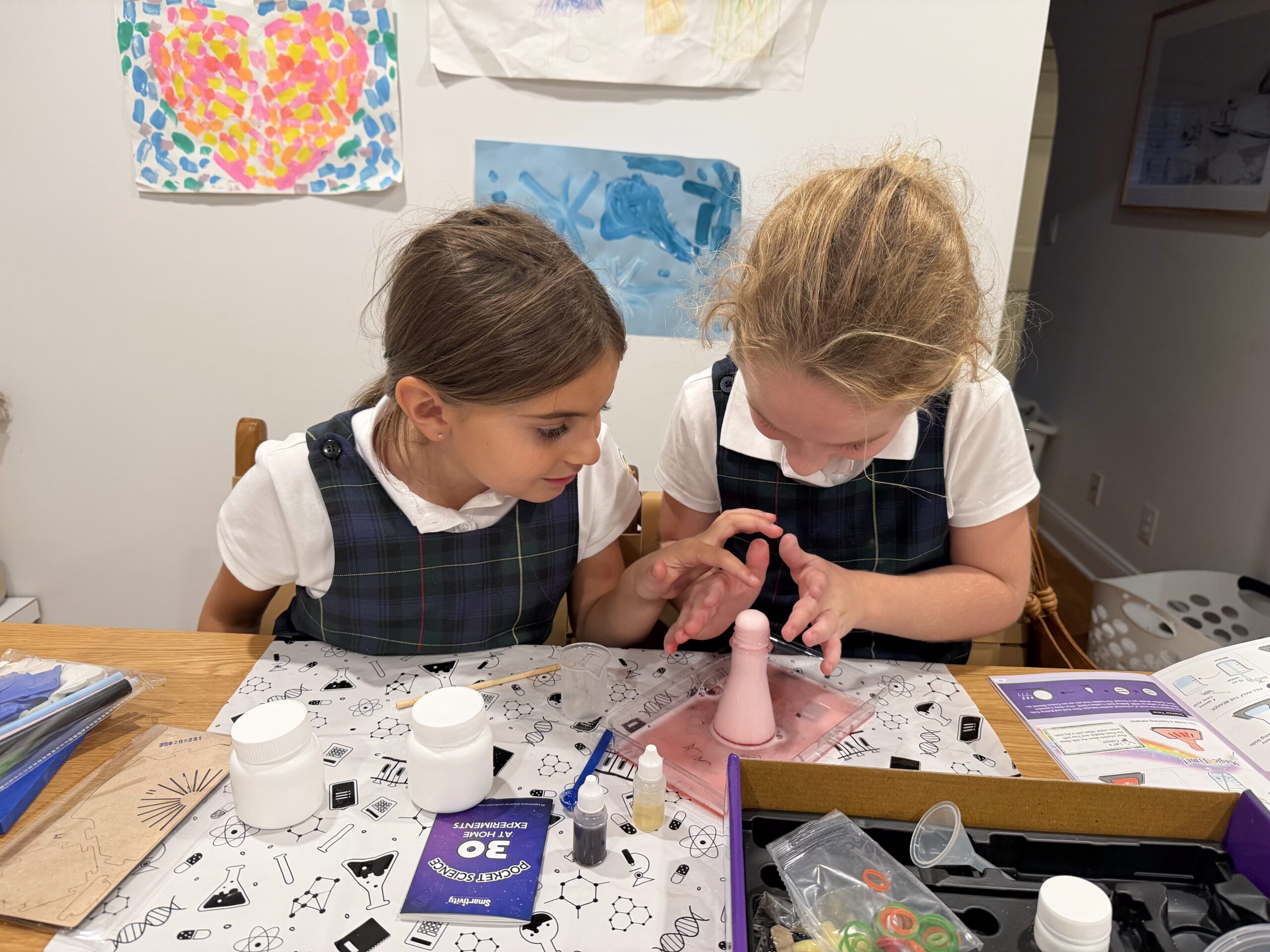 A girl and a girl in school uniforms exploring a science experiment at a classroom table.