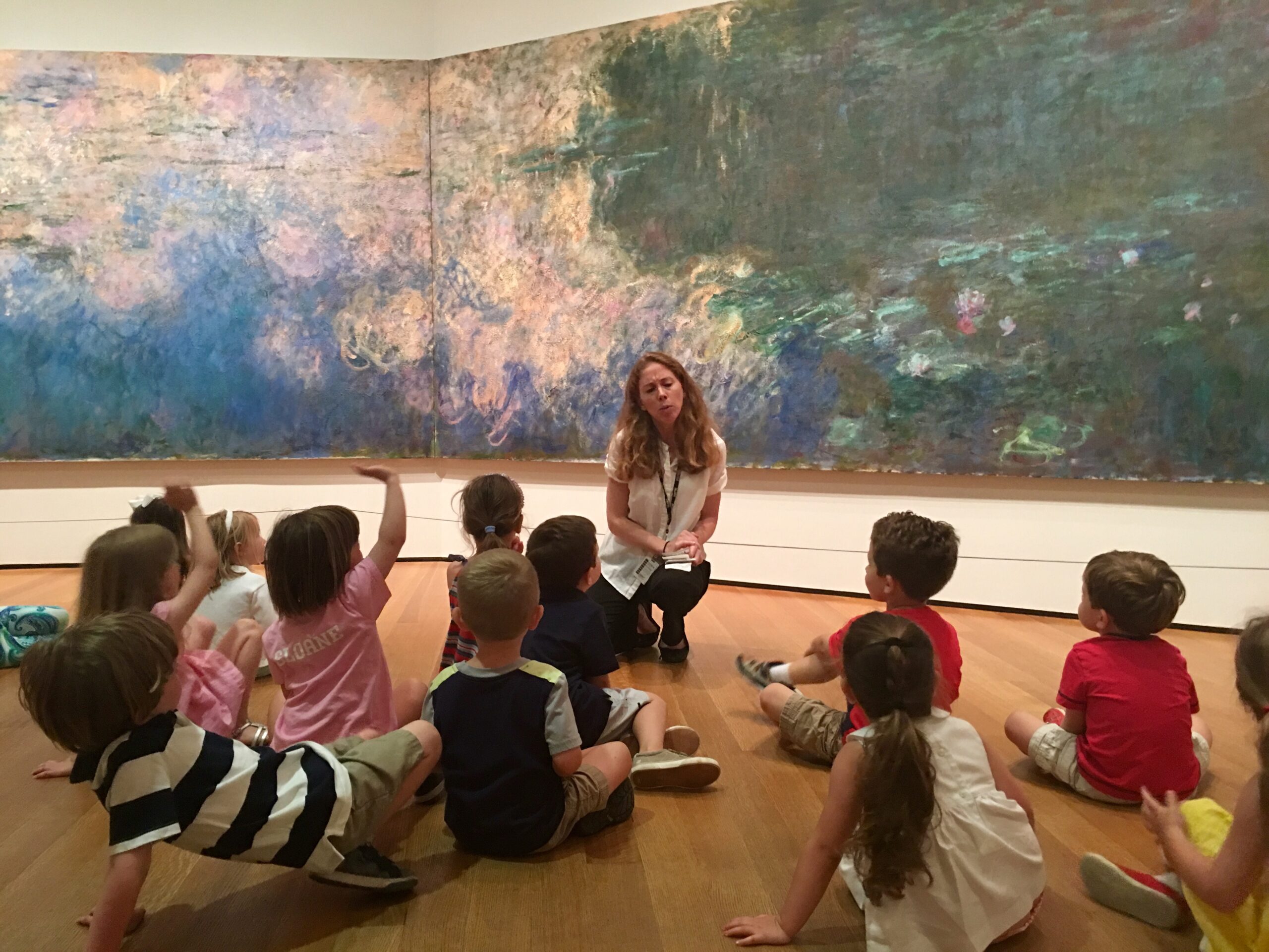 A colorful art gallery with a group of children listening to a woman guide.