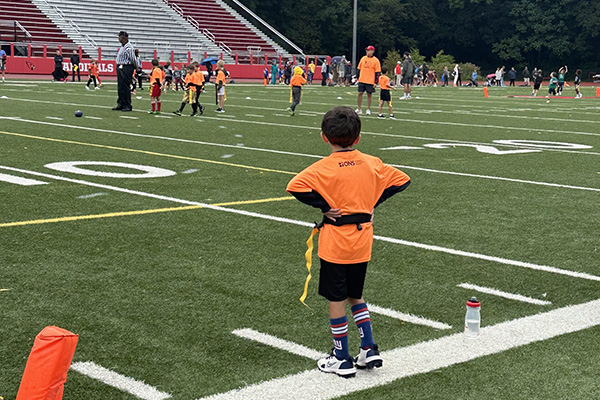A football player in orange jersey standing on a football field during a game or practice session.